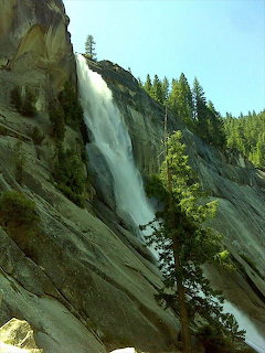 Nevada Falls waterfall flowing down a tall granite rock face with pine trees and blue sky