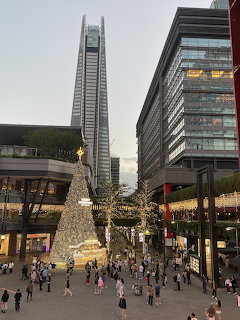 Lit Christmas tree in a busy outdoor shopping plaza with modern buildings in Taipei