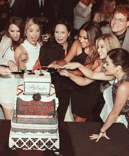 Group of women cutting a red ribbon on a large tiered cake at a celebration event