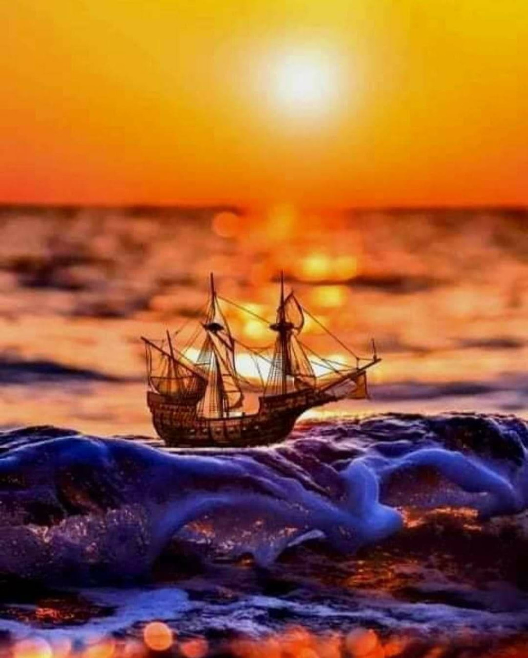 Miniature wooden sailing ship on rocks at sunset with orange sky and ocean backdrop