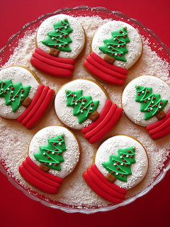 Seven round cookies decorated with green icing Christmas trees and red ribbon designs on a red plate dusted with powdered sugar