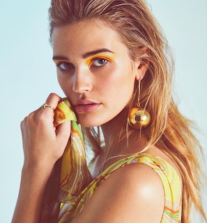 Portrait of woman with blonde hair wearing large gold spherical earrings and yellow striped top