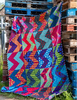 Colorful zigzag patchwork quilt with chevron pattern in bright fabrics hanging on wooden pallet backdrop