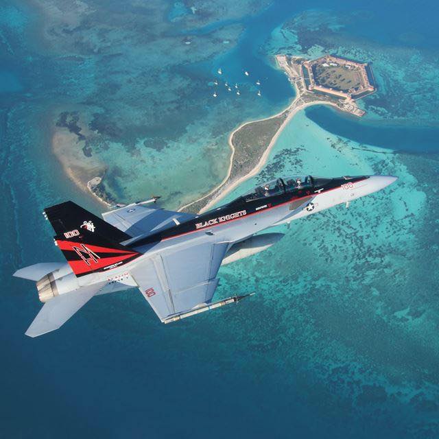 Black Knights F-18 fighter jet flying over a turquoise ocean lagoon and small island