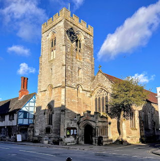 Historic stone church with tall tower and adjacent timber-framed building on sunny day