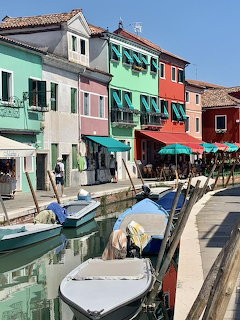 Vibrant multi-colored houses line a canal in Burano with boats moored along the waterfront