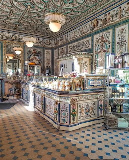 Ornate vintage pastry shop interior with painted tiles, display counter and decorative ceiling.