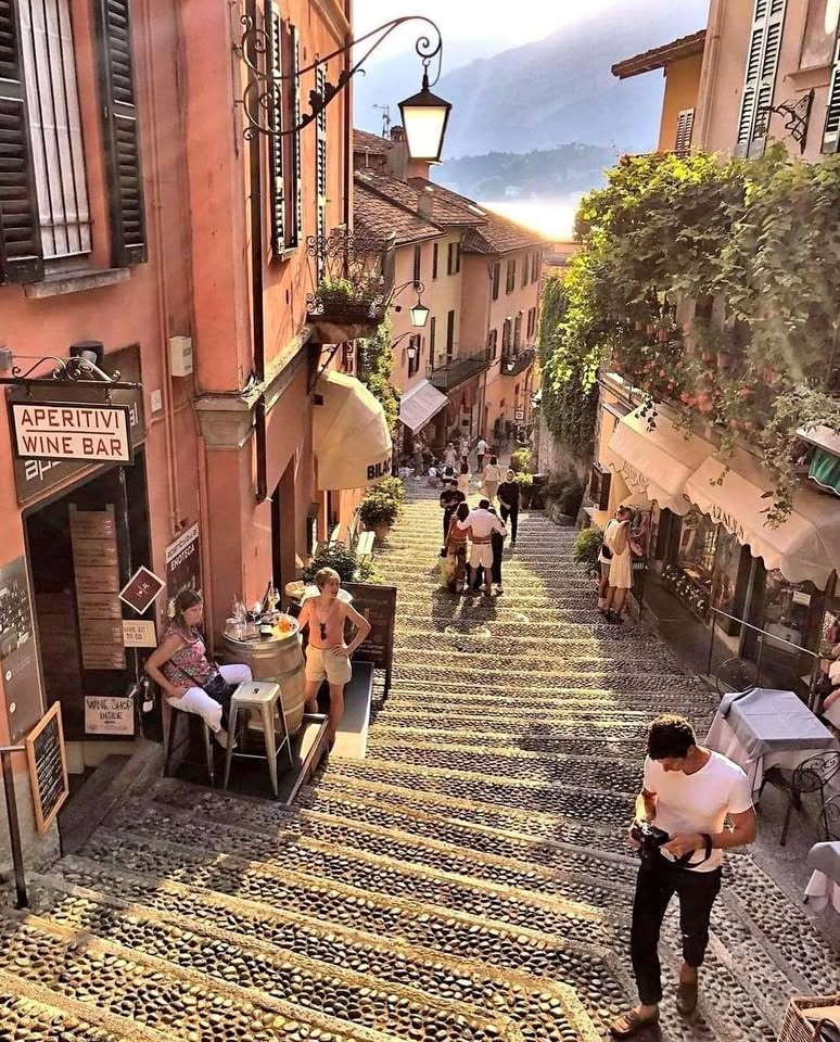 Steep stairway with outdoor cafes descending to Lake Lugano through colorful buildings with mountains in background