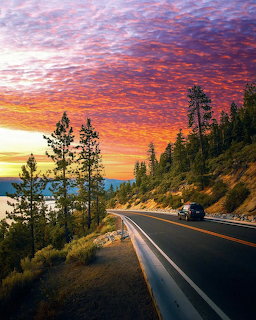 Curved mountain highway at sunset with vibrant orange sky and pine trees on hillside