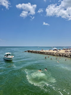 Turquoise ocean water with swimmers, boat, and rocky jetty under blue sky with white clouds