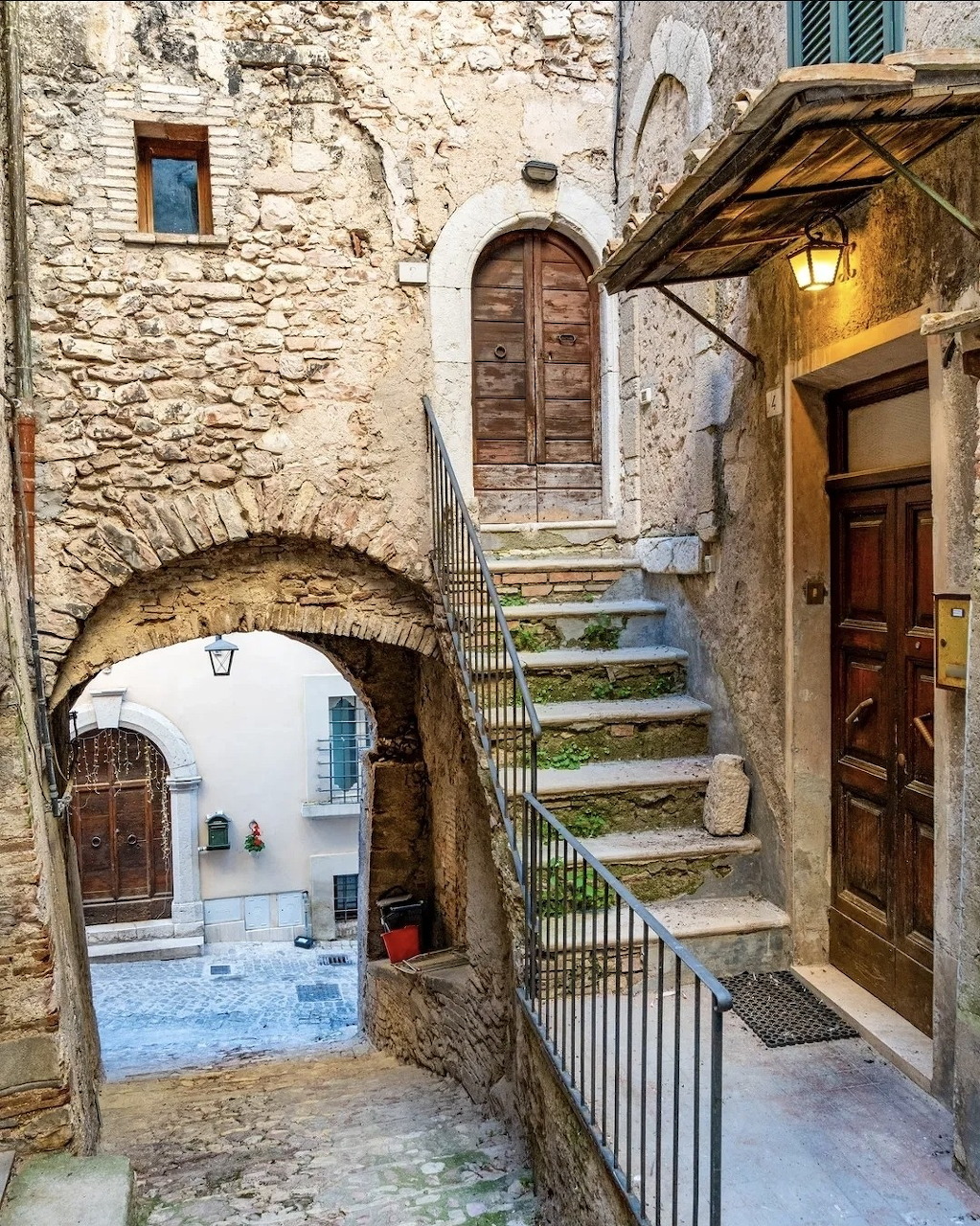 Narrow stone alley in a medieval village with arch, staircase, wooden doors, and lantern