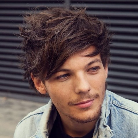 Young man with messy dark hair and stubble wearing a denim jacket, close-up portrait