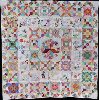 Colorful patchwork quilt with geometric blocks, appliqué flowers, and pieced borders on light fabric