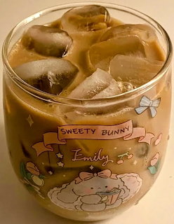 Glass of iced coffee with ice cubes in a cute decorated cup on a beige background