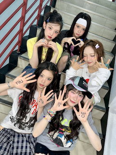 Five young women posing on stairs making hand gestures with Korean text written on their palms