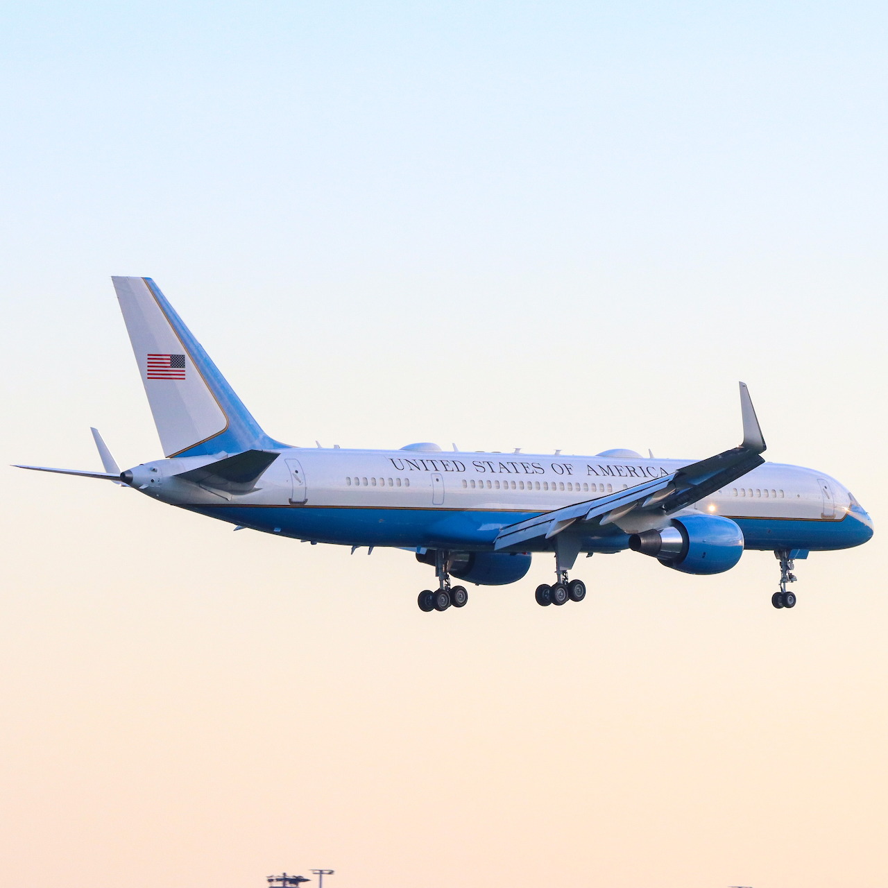 United States Air Force Boeing 757 airplane in flight with landing gear down against a pale sunset sky