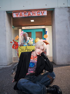 Blond person sitting cross-legged in a doorway under a Vacancy sign