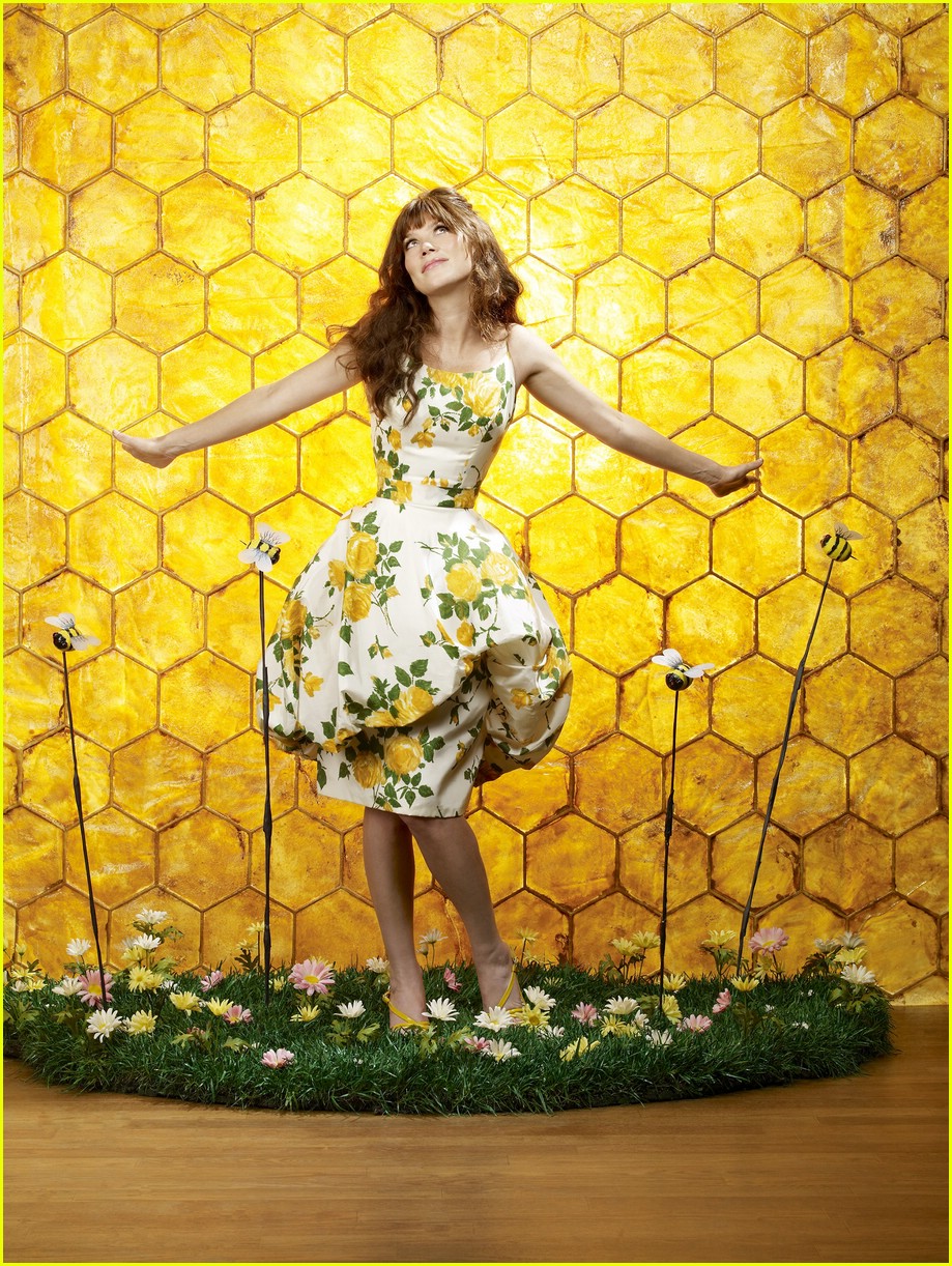 Woman in floral dress standing against yellow honeycomb wall with daisies on ground