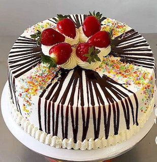 Round cake with white frosting, chocolate stripes, rainbow sprinkles, and strawberry decoration on top