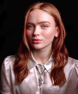 Studio portrait of Sadie Sink with red hair and a satin blouse against a dark background