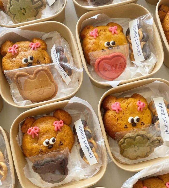 Adorable bear-shaped pastries with smiling faces and pink flower decorations in takeout boxes