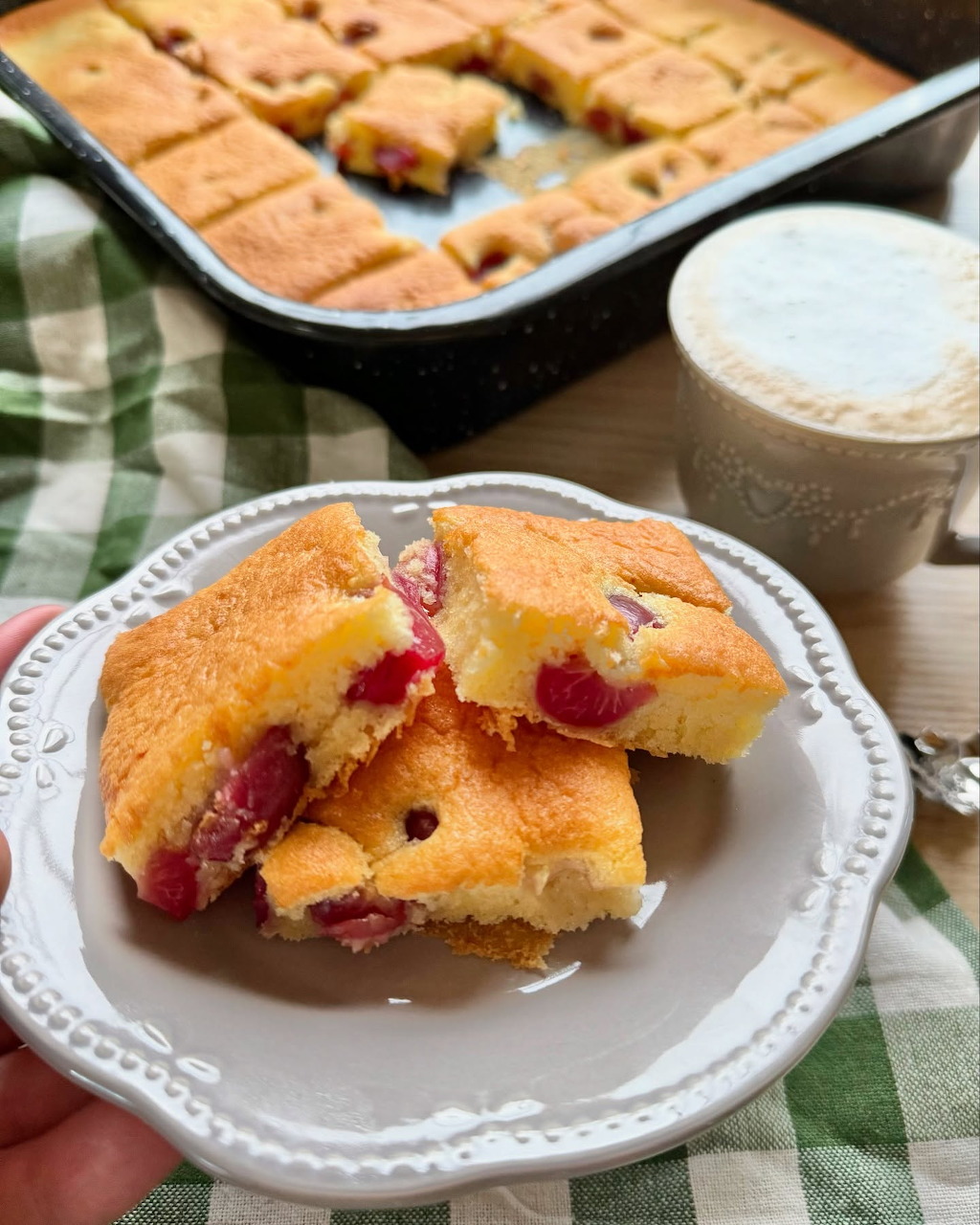 Sliced cherry cornbread squares on a white plate with a baking pan and mug in background