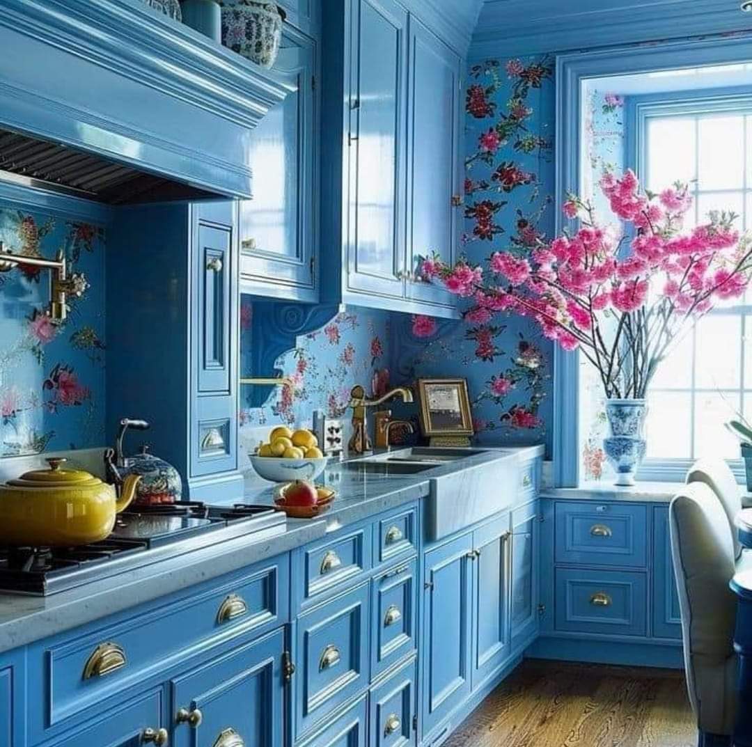 Blue kitchen with floral wallpaper, pink blossoms in a vase, and sunlight by the window