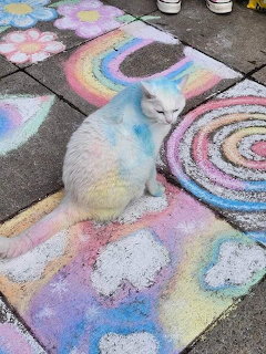White rabbit sitting on vibrant sidewalk chalk art with rainbow colors and spiral patterns