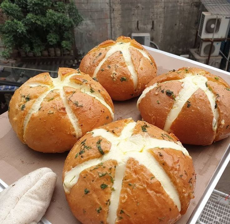 Four round bread buns with melted cheese crosses and herbs on top, on parchment paper