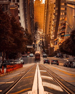 Steep San Francisco street with cable car tracks, cars, and tall buildings at golden hour