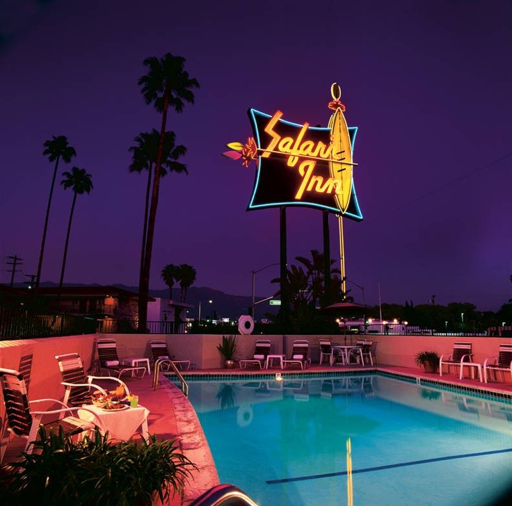 Motel pool at dusk with neon Safari Inn sign, palm trees, and lounge chairs