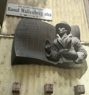 Bronze memorial plaque with sculpture of Raoul Wallenberg seated on wall beneath street sign in Budapest
