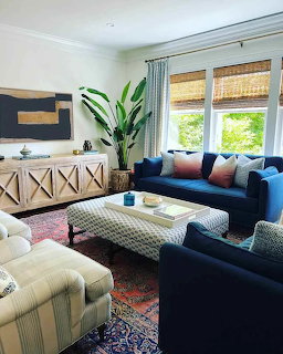 Living room with navy blue sofas, patterned ottoman, tropical plant, and wooden sideboard near large windows