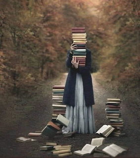 Woman in blue dress holding a tall stack of books on an autumn forest path with scattered books around her