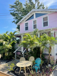 Pink two-story Florida beach house with tropical palms and a small outdoor patio table and chairs