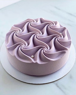 Round lavender frosted cake with piped rosettes on top on a white cake board