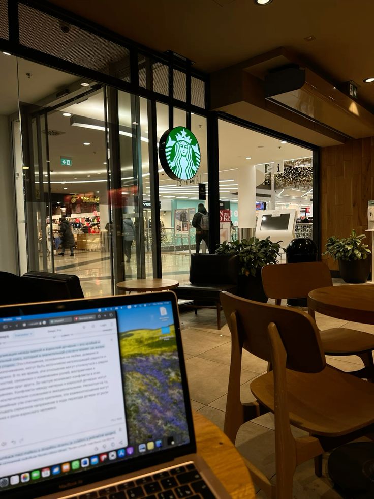 Laptop on table inside a Starbucks café with green logo on glass storefront and wooden chairs