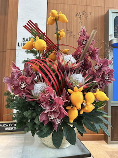 Large indoor floral arrangement with pink lilies, yellow orchids, and green leaves in a white vase