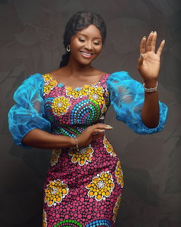 Smiling woman in colorful African print dress with blue puff sleeves waving at camera