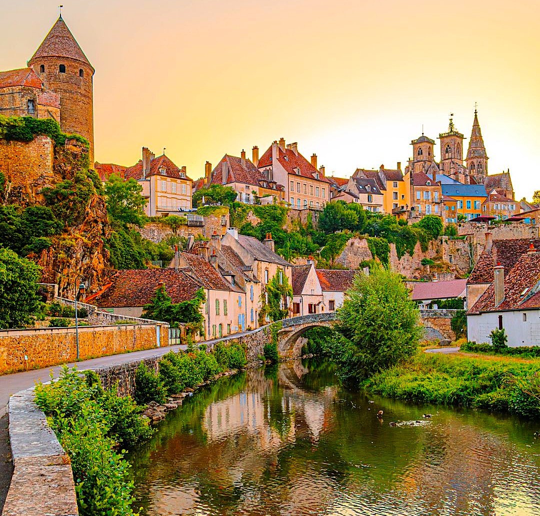 Medieval French village with stone towers and church spires reflected in a canal at golden hour
