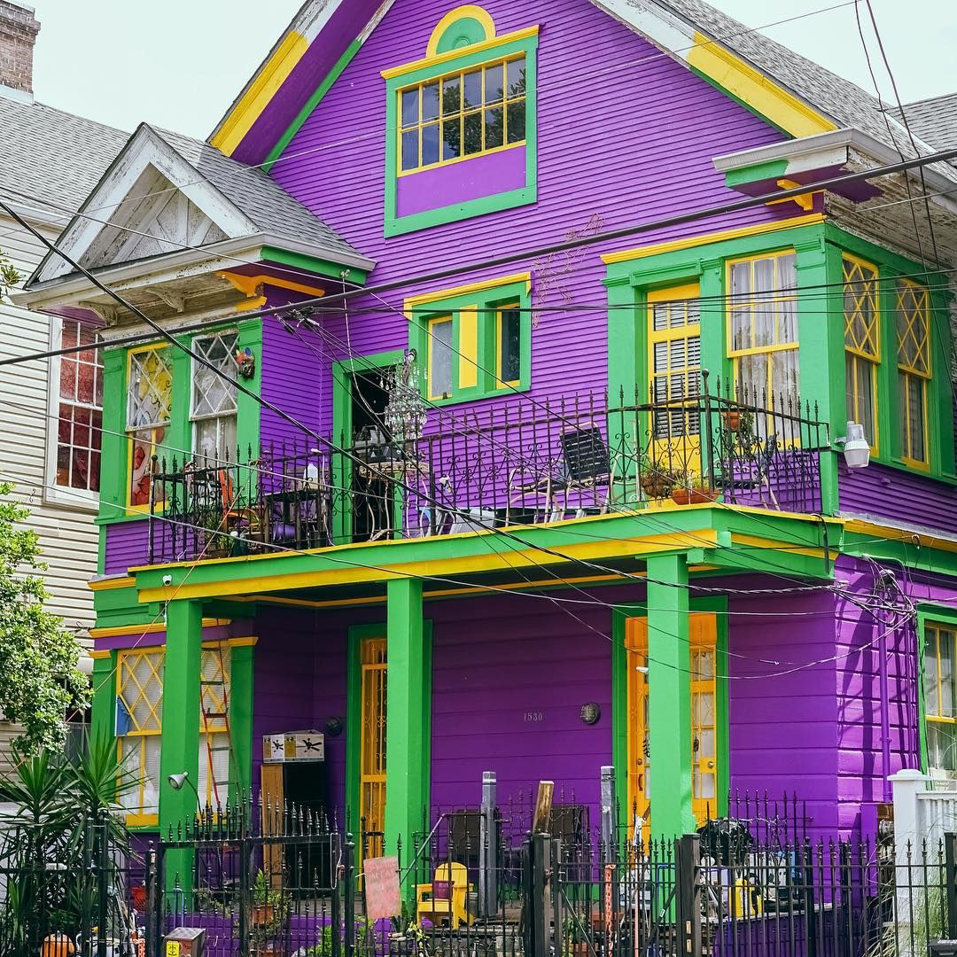 Bright purple two-story house with green and yellow trim, balconies, and a black iron fence