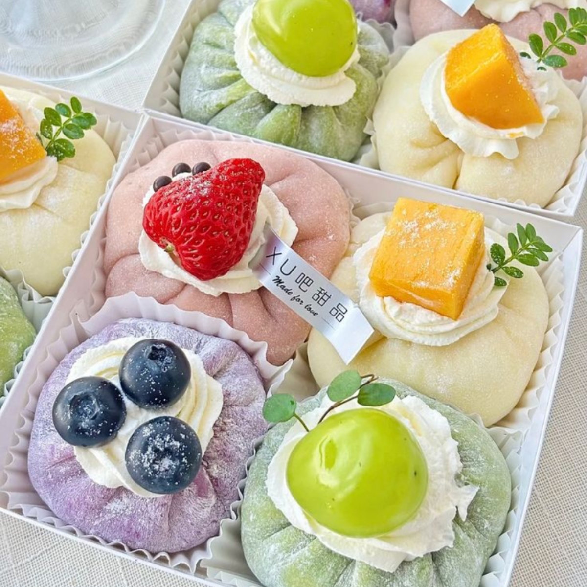 Assorted colorful mochi desserts topped with fresh berries and fruits arranged in a white box