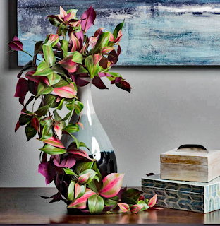 Artificial magnolia flowers in white vase on table with blue abstract painting behind