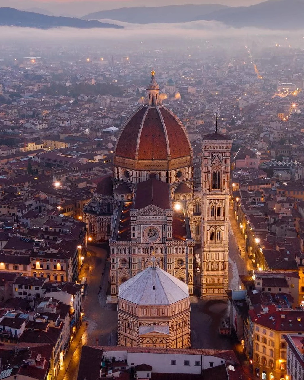 Aerial view of Florence Cathedral with Brunelleschi's dome illuminated at dusk over the city