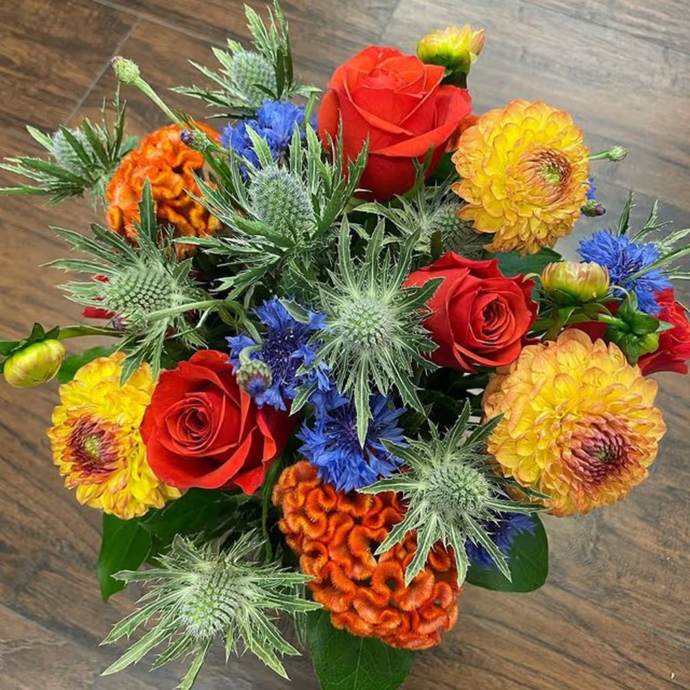 Colorful mixed flower bouquet with roses, dahlias, and thistle on wood table