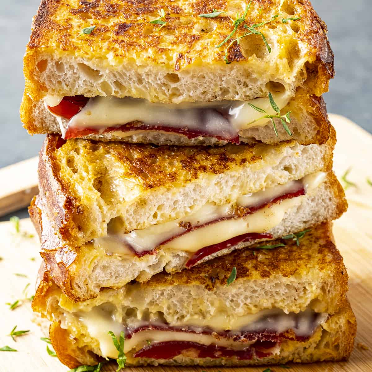 Stack of toasted ham and cheese sandwiches with melted cheese on a wooden board