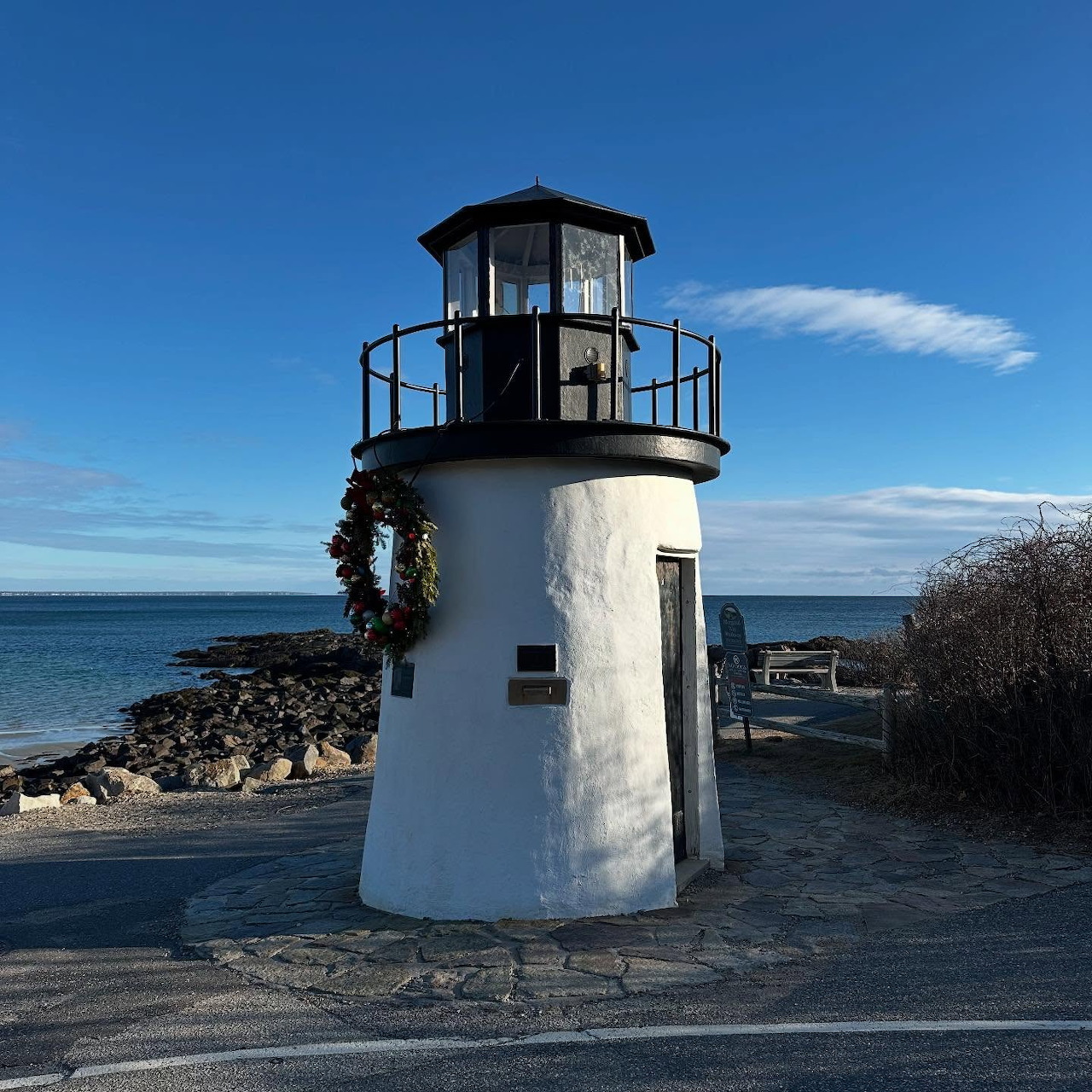 White lighthouse with black top on rocky coast under blue sky in Ogunquit, Maine
