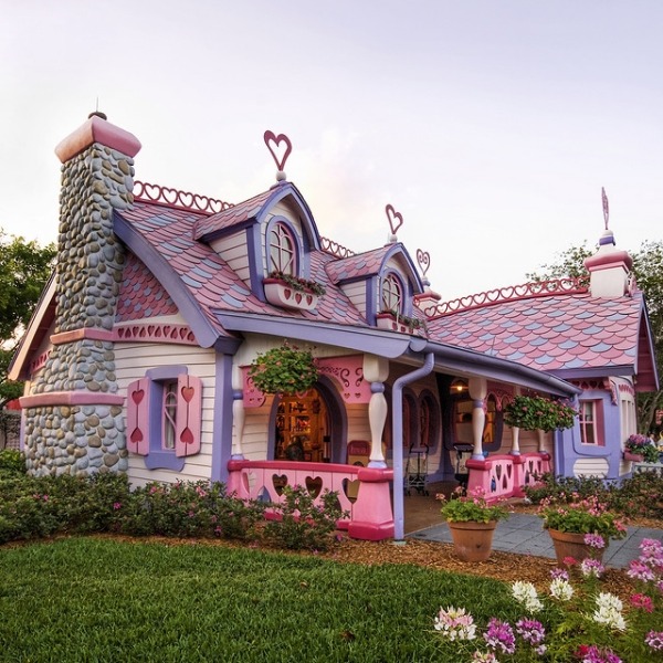 Whimsical pink cottage with stone chimney, heart accents, and flower garden