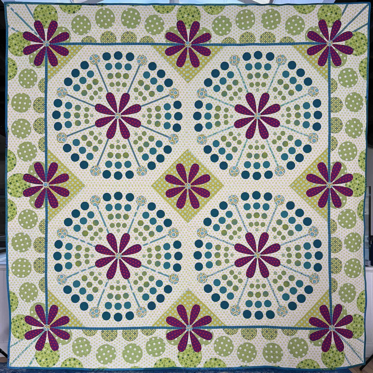 Quilt with repeating circular purple flower motifs and blue-green dots in radiating patterns with floral border