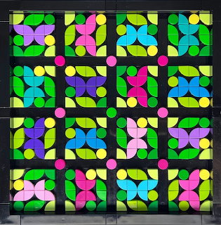 Grid of colorful stained glass panels with geometric circular and oval shapes in bright colors separated by black frames